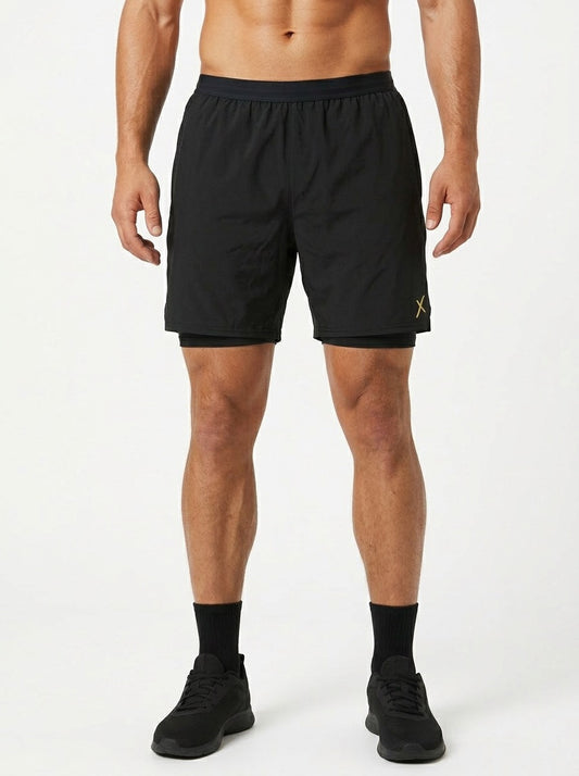 ABXCORE black training shorts worn by a man from the front, yellow logo visible on the leg, black sneakers and socks on a white background.