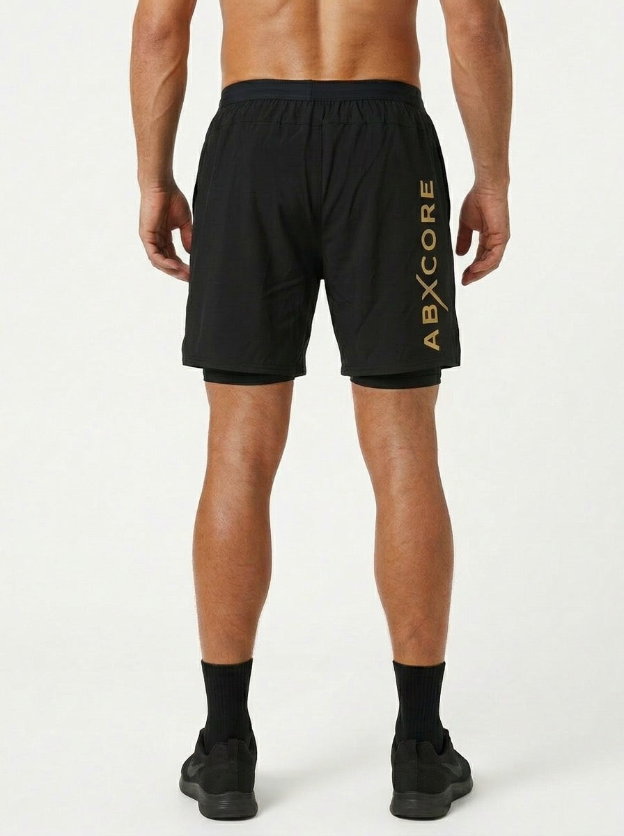 ABXCORE black training shorts seen from the back, large vertical yellow ABXCORE logo on the leg, man wearing black sneakers and socks on a white background.