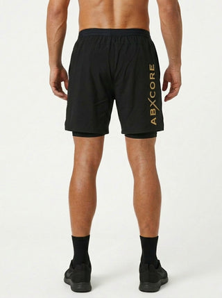 ABXCORE black training shorts seen from the back, large vertical yellow ABXCORE logo on the leg, man wearing black sneakers and socks on a white background.